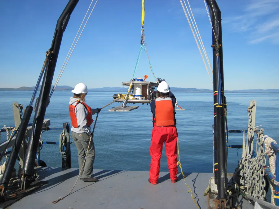Dua peneliti menurunkan instrumen ADCP dari geladak kapal survei di San Pablo Bay